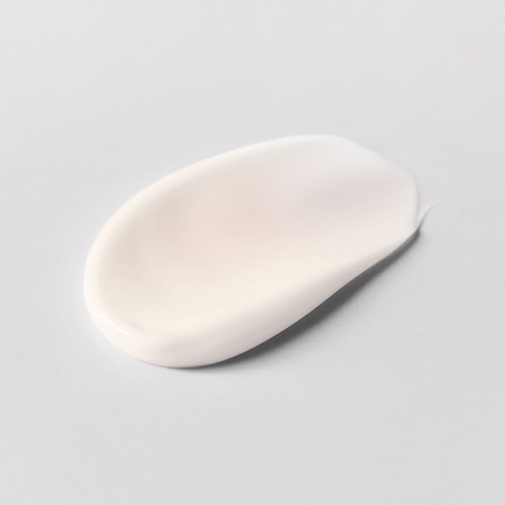 Ein ovaler Klecks weißer Creme auf einer glatten, grauen Oberfläche.
