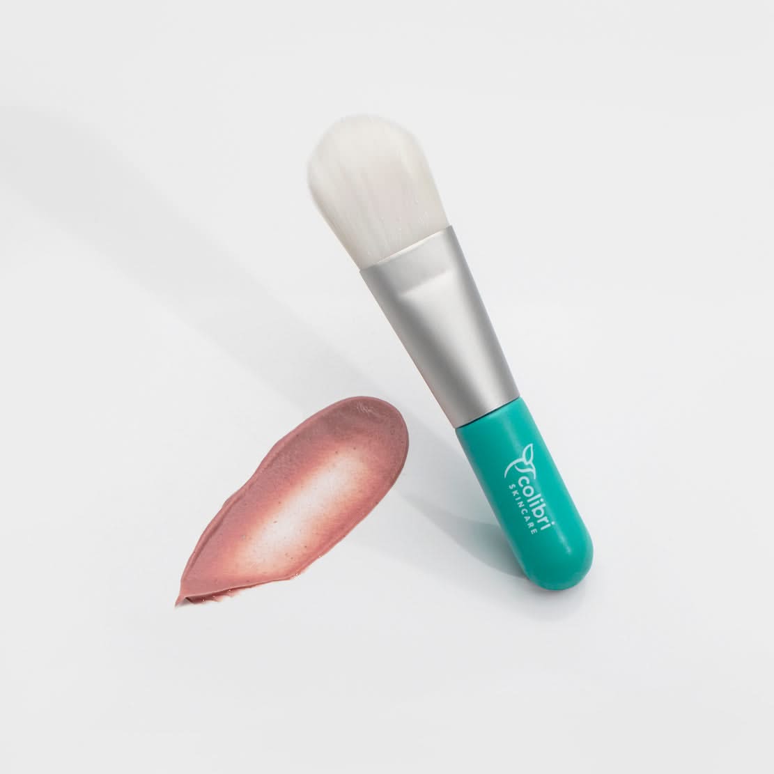 Make-up-Pinsel mit türkisfarbenem Griff und einem rosa Cremestreifen auf weißem Hintergrund.