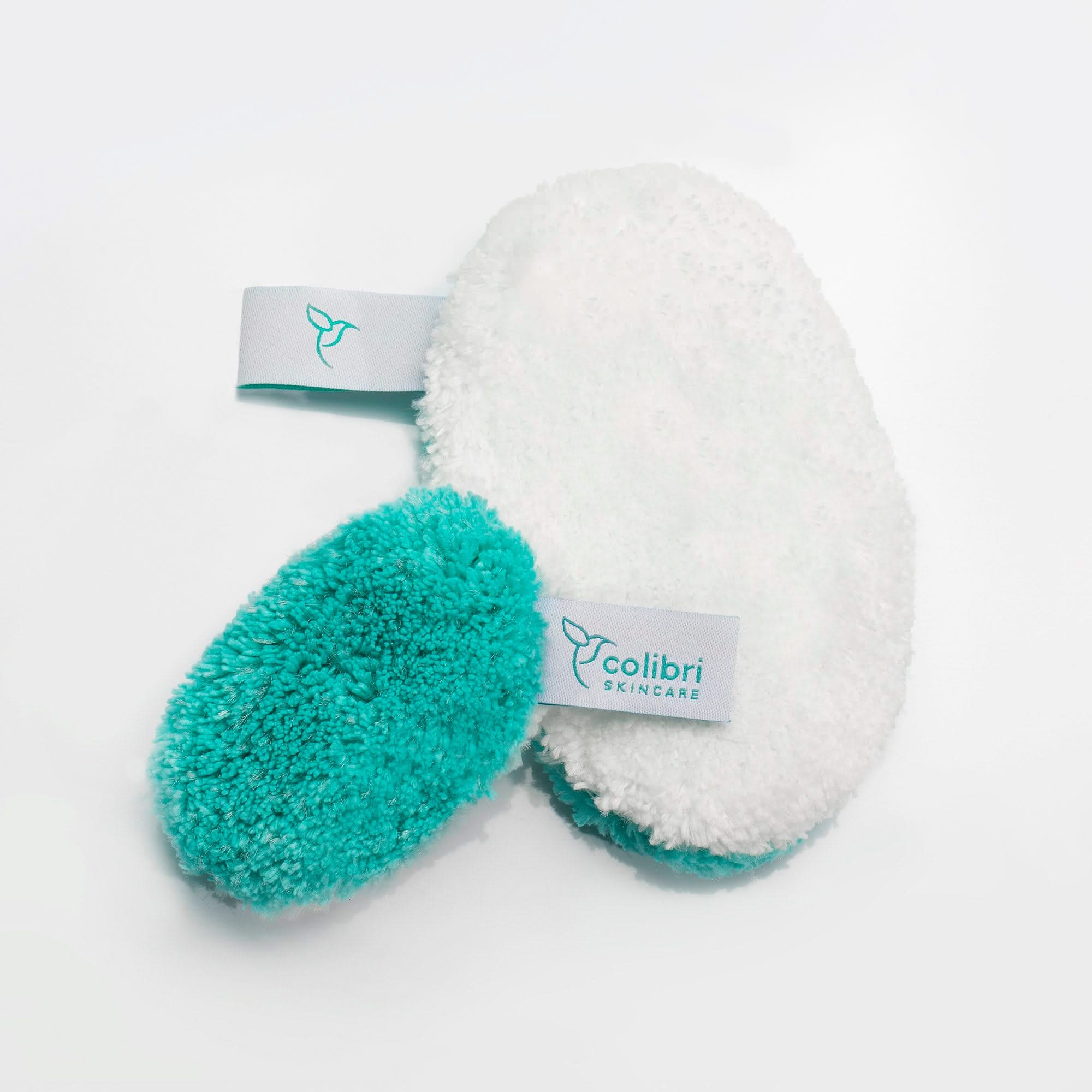 Zwei flauschige Reinigungspads, eines in Weiß und das andere in Türkis, mit dem Logo "colibri SKINCARE".