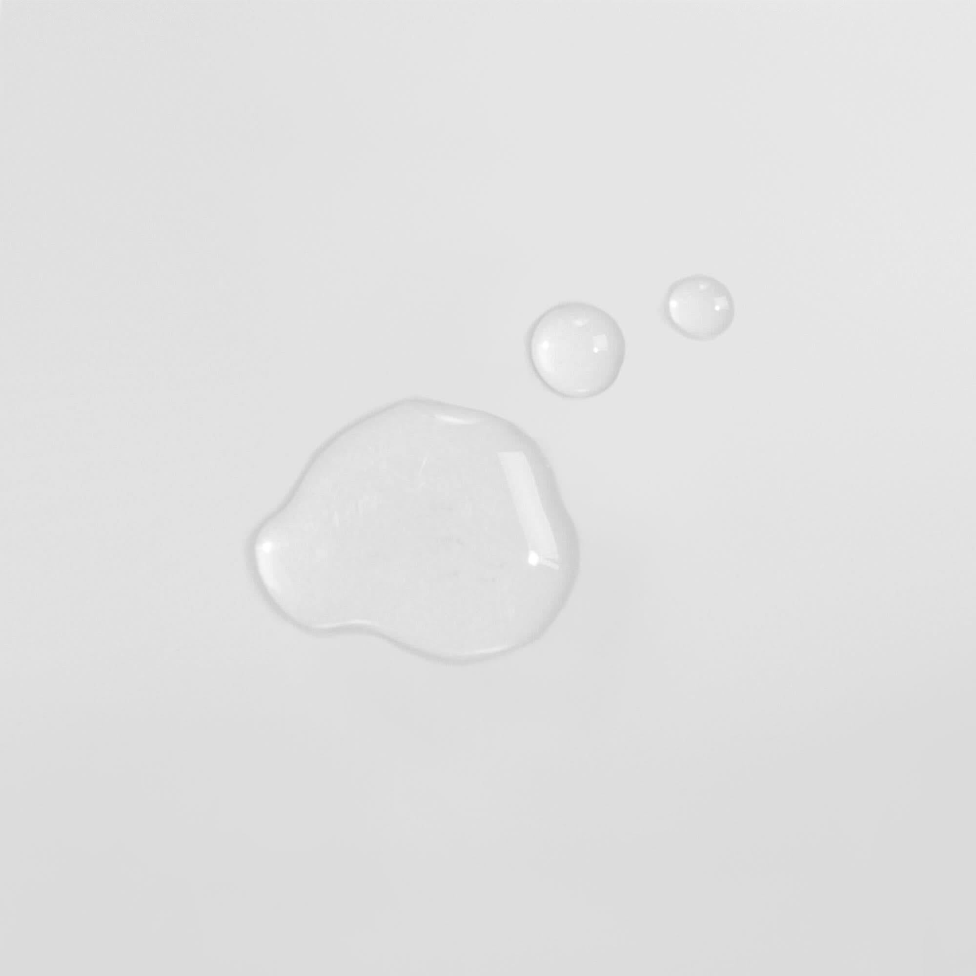 Drei Wassertröpfchen auf einer weißen Oberfläche, zwei kleinere oben rechts und ein größeres links unten.