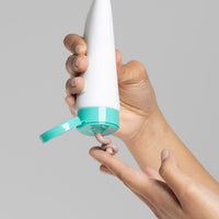 Eine Person drückt eine hellbraune Creme aus einer weißen Tube mit türkisfarbenem Deckel auf ihre Finger.